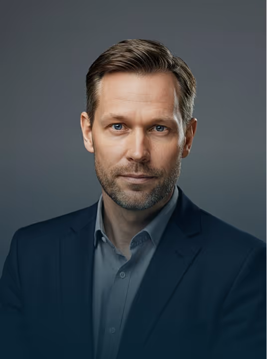 Portrait of a middle-aged man in a dark suit and light shirt against a plain gray background.