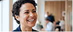 Smiling woman with short curly hair in a professional setting with blurred people in background.